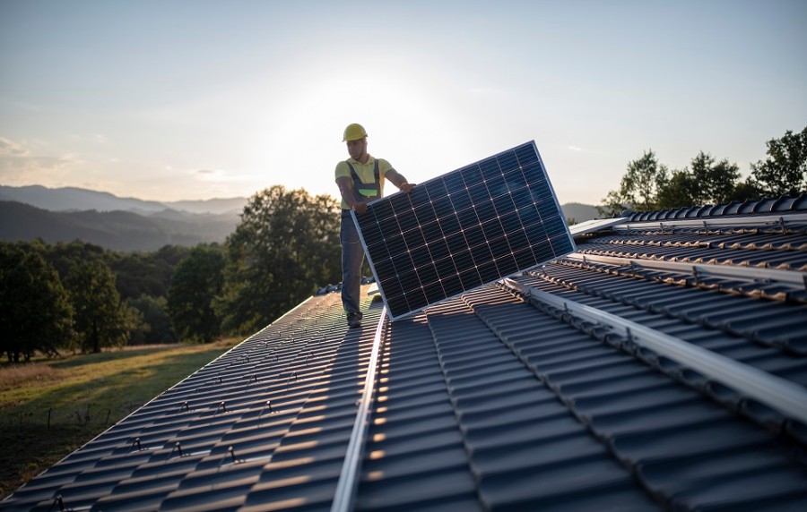 Ein Mann verlegt auf dem Dach eines Hauses Solarpanels.
